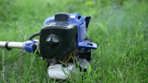 Running brushcutter trimmer on a green blurry background on a sunny summer day photo