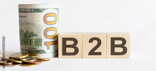 B2B written on a wooden cube with coins and dollars