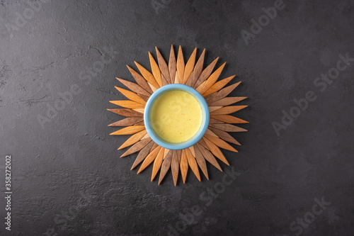 Ceramic blue cup with traditional Indian masala chai tea on a bamboo stand in the form of the sun on a dark background. Top view with copy space