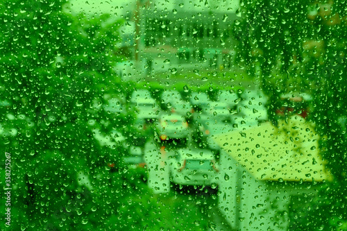 Drops of water on the glass with a touch of green. Water drops with space for design and text. Drops of water on a background of trees and cars.
