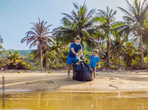 Young happy family activists collecting plastic waste on beach. Dad and son volunteers clean up garbage. Environmental pollution problems. Outdoor lifestyle recreation. Natural education of children