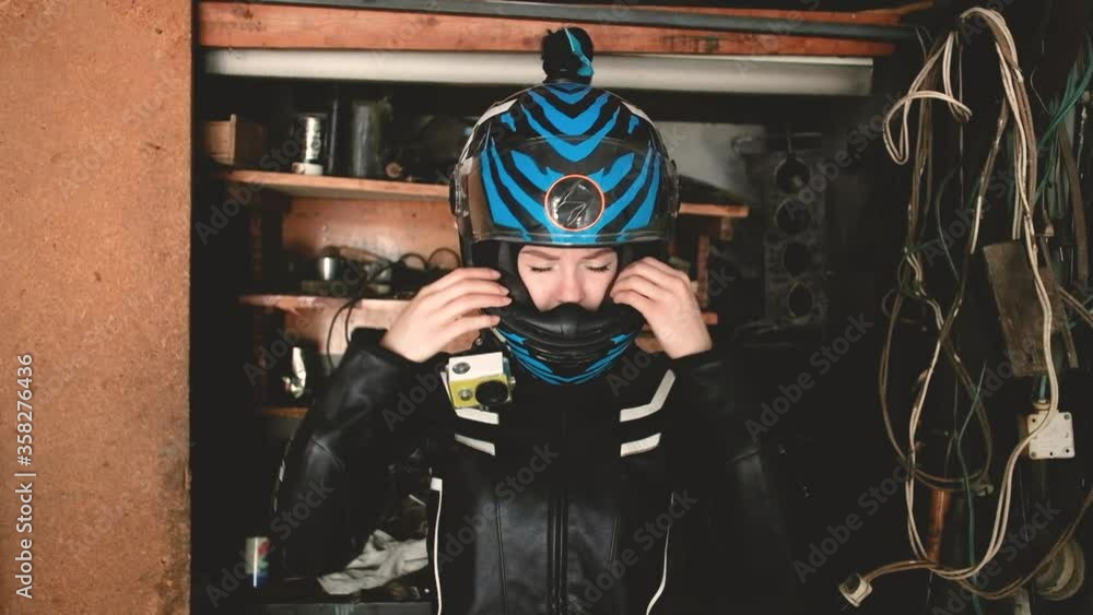 beautiful woman motorcyclist puts on a helmet in the garage. The concept of security, an active lifestyle, speed and freedom. Fashionable motorcycle equipment. Lovely girl 20-25 years old. beautiful woman motorcyclist puts on a helmet in the garage. The concept of security, an active lifestyle, speed and freedom. Fashionable motorcycle equipment. Lovely girl 20-25 years old.