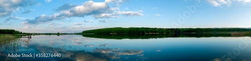 Panoramic landscape from the lake shore with colorful clouds in the spring sun. © mikhailgrytsiv