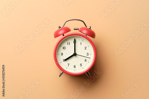 Red vintage alarm clock on pastel orange paper background.