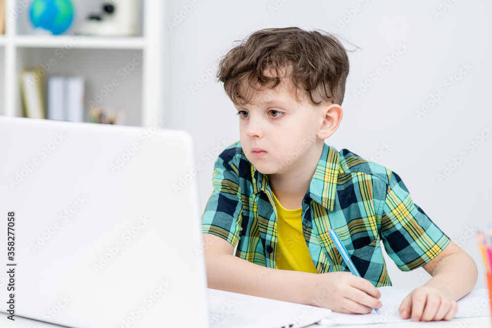 Young boy is doing homework with paltop and writing to notebook at home. Distance education during quarantine Young boy is doing homework with paltop and writing to notebook at home. Distance education during quarantine