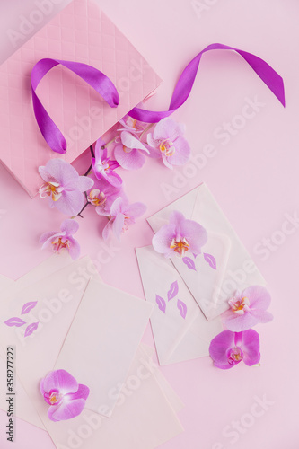 Pink gift bag and flying orchid flowers on light pink background. Top view greeting card with flowers. Holiday, Women's day, mother's day greeting concept.