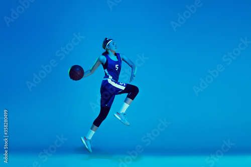 In high flight. Young caucasian female basketball player training, prcticing with ball isolated on blue background in neon light. Concept of sport, movement, energy and dynamic, healthy lifestyle.