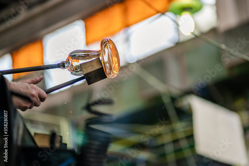 Close-up on the hand of a glassblower artist shaping the molten glass extracted from the furnace in a glass factory where each piece is manually made by the artisans hands. Copy space.