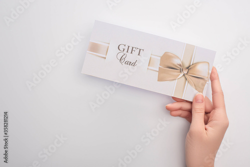 Fotografie Cropped view of woman holding gift card with bow on white background