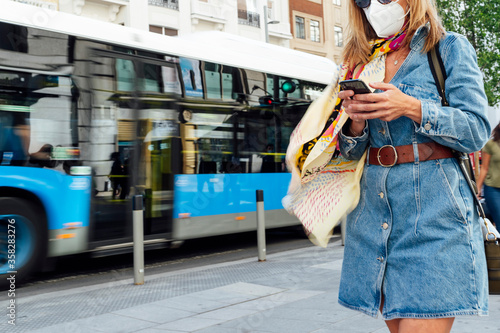 Woman using mobile phone in the street. She is wearing a protective mask for the prevention of a virus. Coronavirus concept