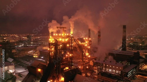 Aerial view of metallurgical plant blast furnace at night with smokestacks and fire blazing out of the pipe. Industrial panoramic landmark with blast furnance of metallurgical production