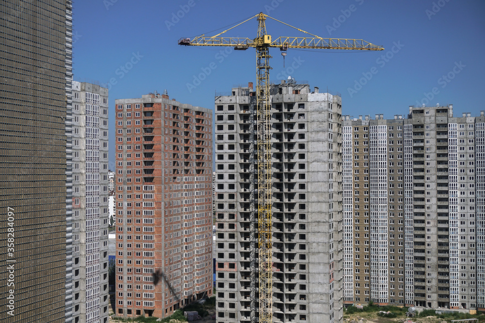 Fototapeta premium Multi-stage construction during the construction process with a yellow crane. Industrial background for design.