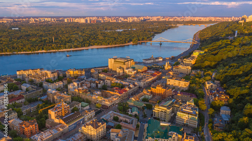 Kyiv (Kiev) city the capital of Ukraine Podol area Sahaidachnoho Street and river Dnipro aerial drone view from the top. Sunset summer beautiful warm light. pedestrian bridge to Trukhaniv Island. 