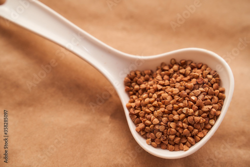 buckwheat lies in a white plastic spoon on a brown background. close up