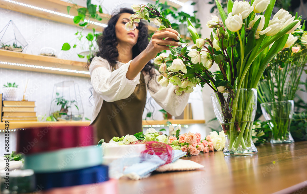 Attractive young woman florist is working in a flower shop.