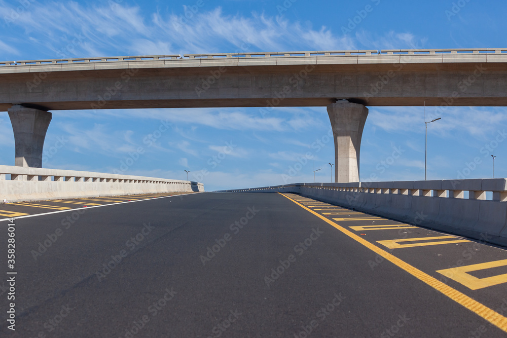 Naklejka premium Travel Route New Road Highway Exit Entry overpass lanes standing middle of empty ramp tarred asphalt road panoramic landscape with blue sky.