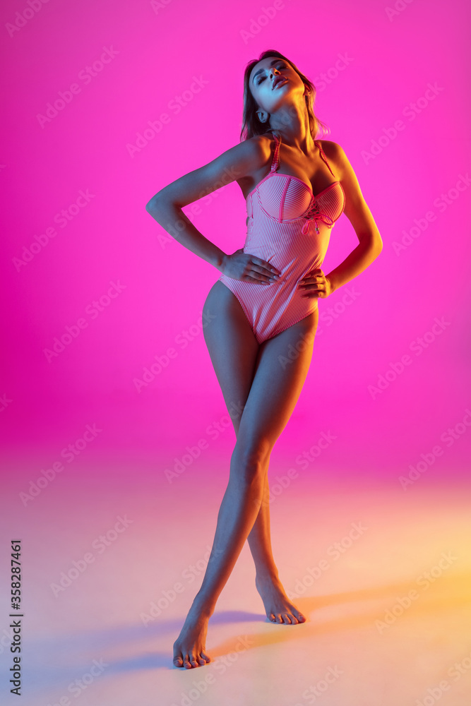 Posing sensual. Beautiful young girl portrait on gradient studio background in neon light. Woman in fashionable bodysuit. Facial expression, summer, weekend, beauty, resort concept. Vacations. Posing sensual. Beautiful young girl portrait on gradient studio background in neon light. Woman in fashionable bodysuit. Facial expression, summer, weekend, beauty, resort concept. Vacations.