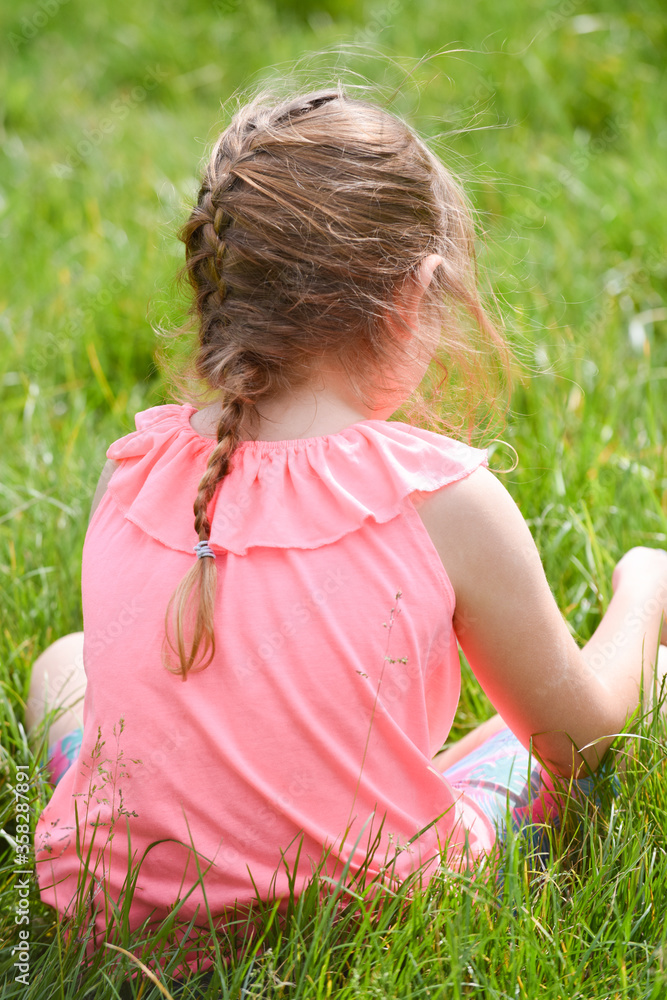 Child sitting in a field of grass outside on summer day
