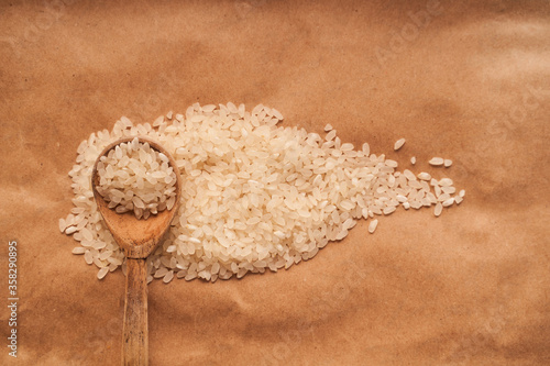 White rice is scattered on a brown background with a wooden spoon and against the other croup. cpy space photo