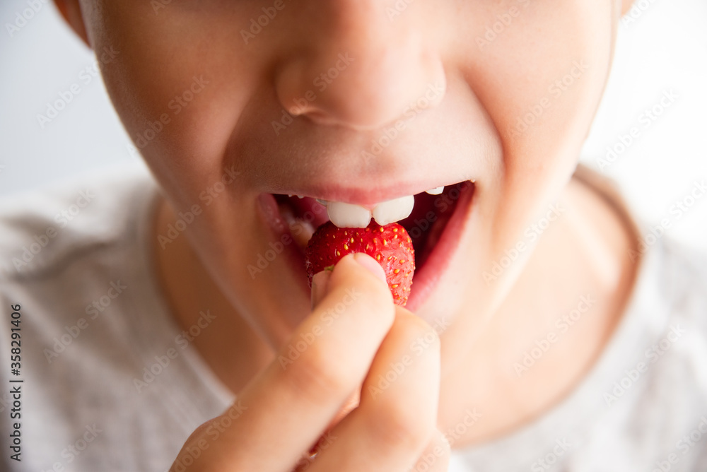 boy eating a very tasty strawberry on a light background. Close up boy eating a very tasty strawberry on a light background. Close up