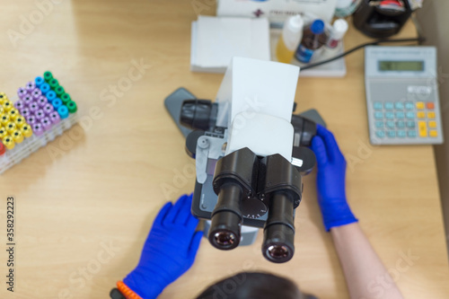 laboratory assistant is looking through a microscope. Close-up doctor laboratory assistant looking through a microscope, determining a blood test of a patient, red blood cells