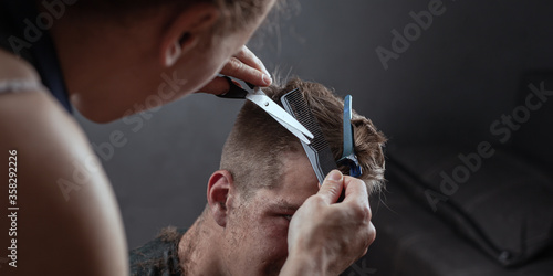 hairdresser cuts hair with scissors on gray background, barbershop