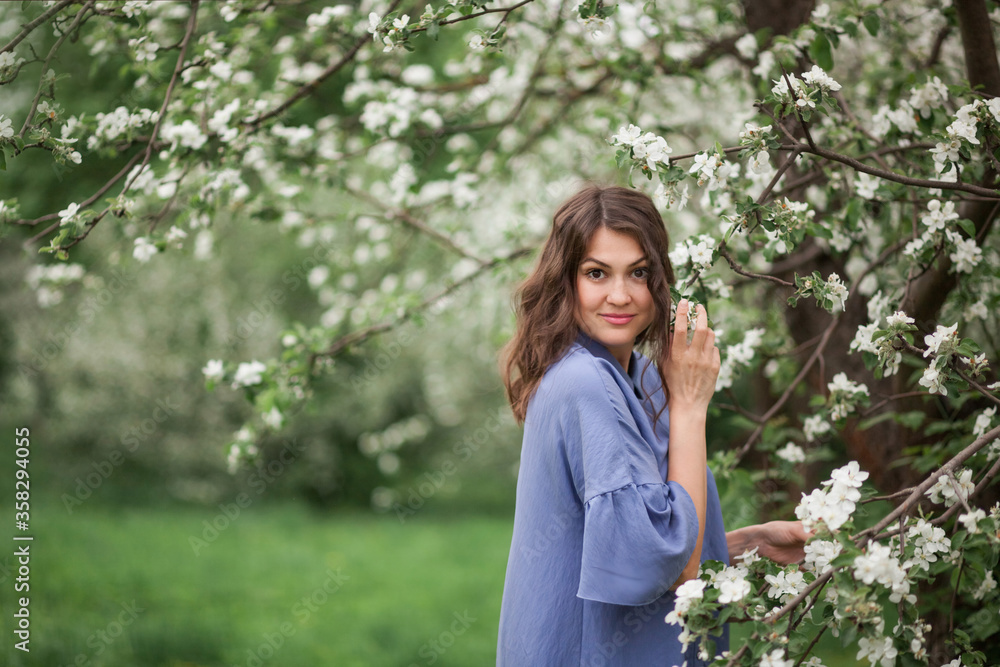 Beautiful girl in a summer dress in a blue hue next to a blossoming apple tree branch. The concept of spring, beauty. Beautiful girl in a summer dress in a blue hue next to a blossoming apple tree branch. The concept of spring, beauty.