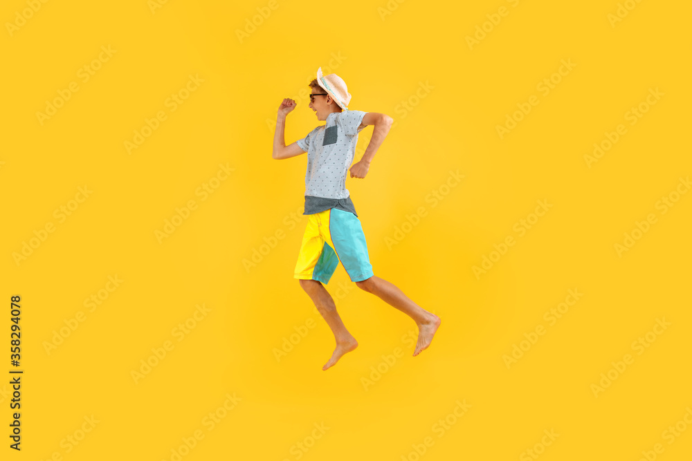 happy excited teenager in sunglasses and a summer hat, having fun and jumping, on a yellow background happy excited teenager in sunglasses and a summer hat, having fun and jumping, on a yellow background