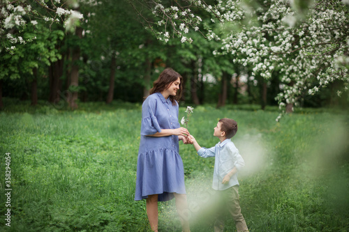 Happy and beautiful mother and son in clothes of blue tones walking in a blossoming apple orchard. The concept of spring, motherhood, happy family, relationships.