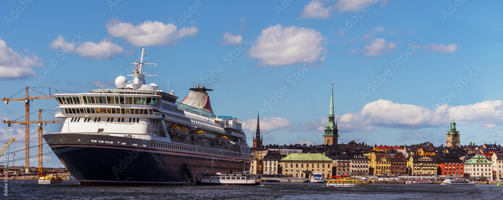 Fototapeta premium Panoramic view of Stockholm, Sweden. The view from the water. A large passenger cruise ship. A beautiful European city under a blue sky with white clouds.