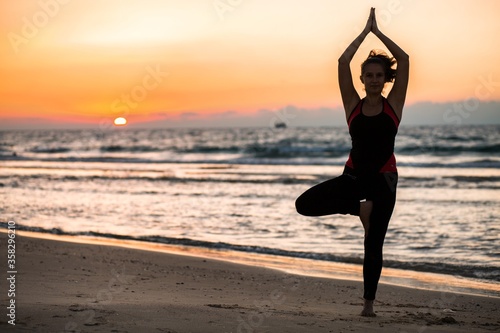 Woman doing yoga at the beach at sunset