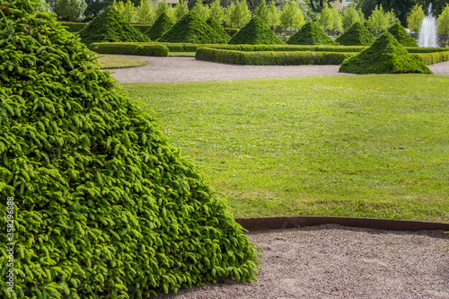 Uppsala, Sweden - 16 June 2019: Beautiful green park with green pyramids of trees and a fountain, in front of the building Linneanum orangery. One of the oldest botanical gardens in the world.
