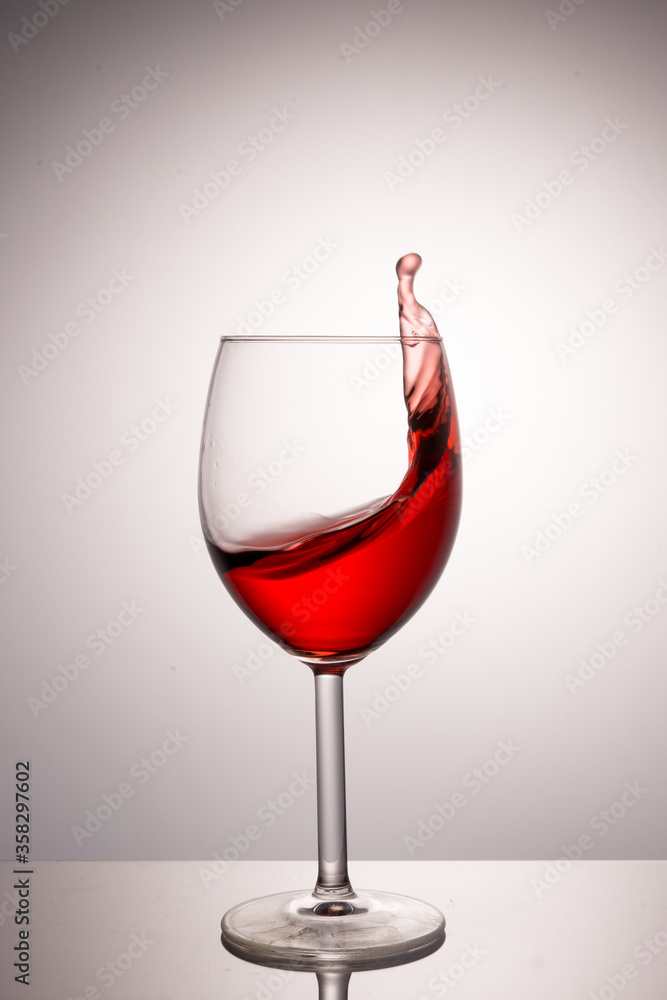 A splash of red wine in a glass on a white background A splash of red wine in a glass on a white background