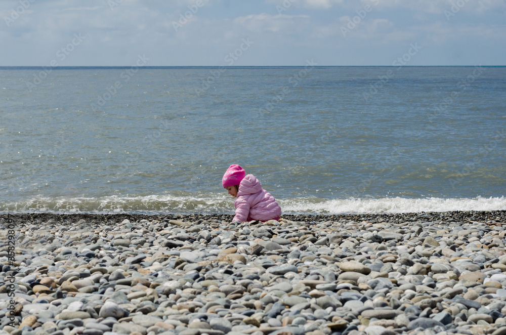 little girl on a stone beach at sea in spring