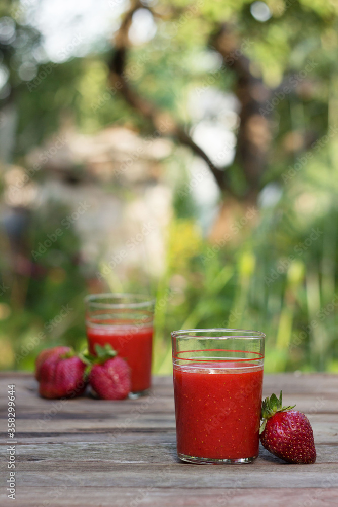 Strawberry juice with glass glasses on a wooden table and on the background of a green garden, on the table are ripe strawberries. Useful food, background, place for text. Strawberry juice with glass glasses on a wooden table and on the background of a green garden, on the table are ripe strawberries. Useful food, background, place for text.