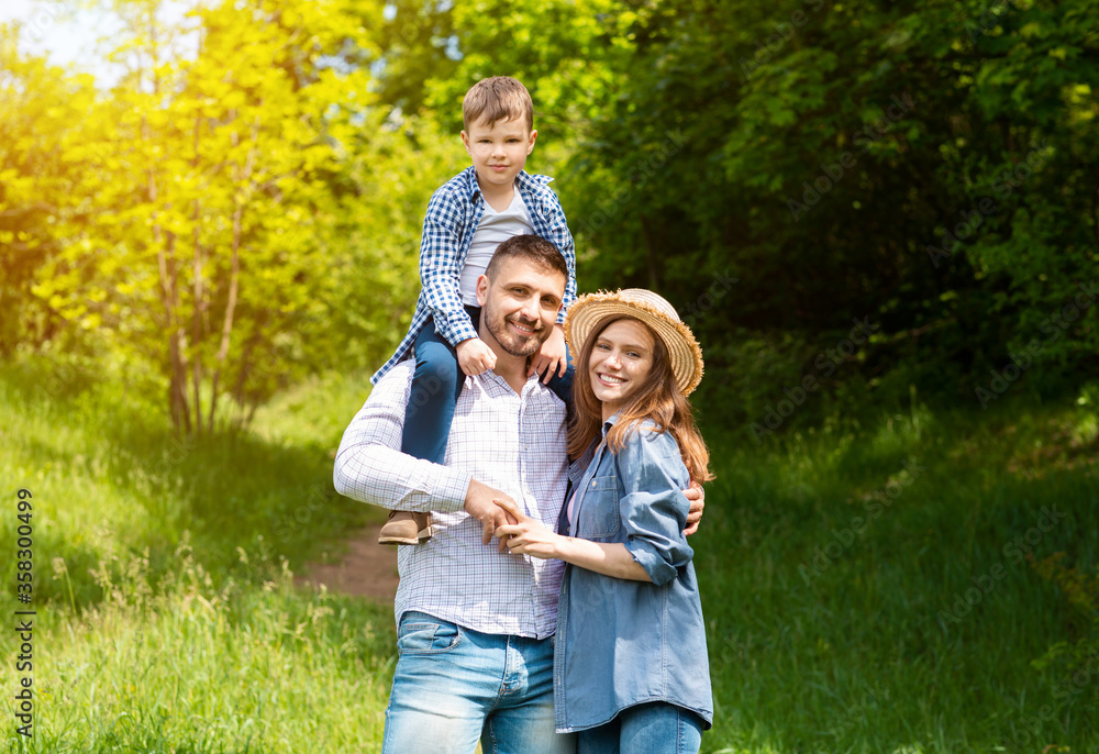 Portrait of loving parents with their little son standing together in forest on sunny day Portrait of loving parents with their little son standing together in forest on sunny day