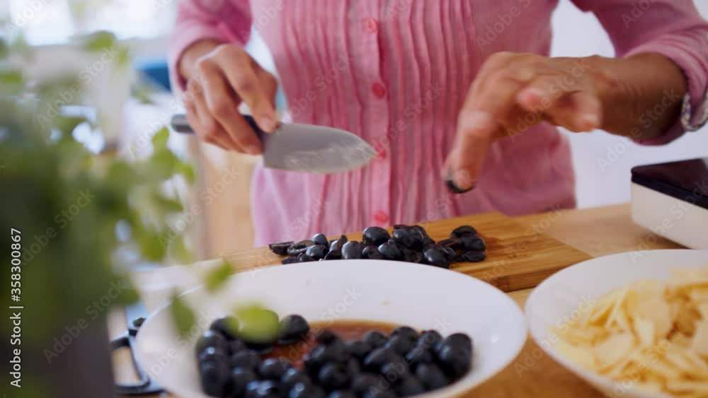 Unrecognizable woman cooking in kitchen indoors, chopping olives. Unrecognizable woman cooking in kitchen indoors, chopping olives.