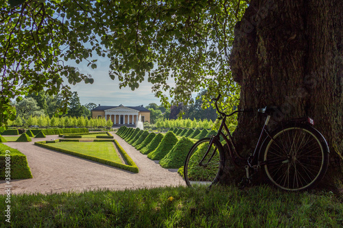 Photography Uppsala, Sweden - 16 June 2019: Beautiful green park with green pyramids of trees and a fountain, in front of the building Linneanum orangery