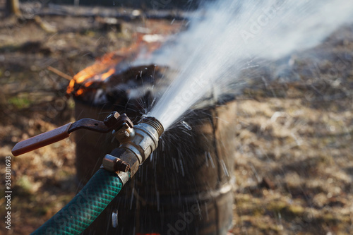 Water spraying from water hose near fire burning in old rusty barrel