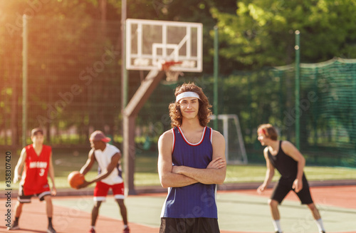 Portrait of positive basketball player and his team playing ball at outdoor court