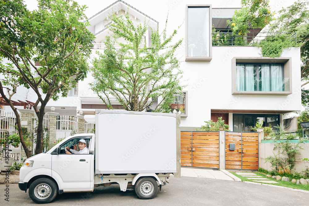 Horizontal long shot of modern Asian delivery man wearing white clothes driving van on sunny day, copy space