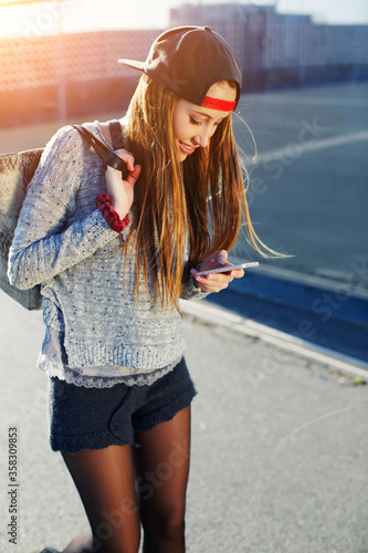 Pretty girl walking outdoors in the street while using busy a smart phone, gorgeous young woman wearing casual spring clothes walking down a city street while texting on her cell phone, flare sun