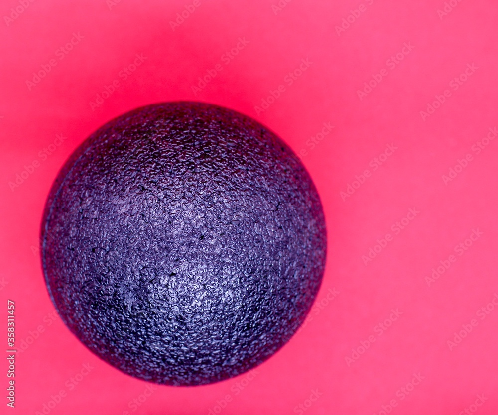 Black fascia ball on a red background from above. Massage ball made of polystyrene for fascial release Black fascia ball on a red background from above. Massage ball made of polystyrene for fascial release