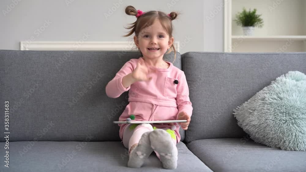 Curious cute baby girl using tablet. Lying on sofa alone. Little child playing funny games app at home. Curious cute baby girl using tablet. Lying on sofa alone. Little child playing funny games app at home.