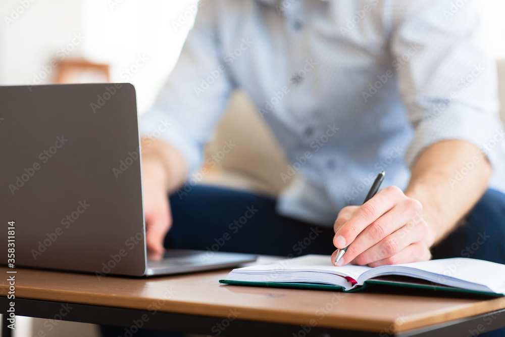 Man using laptop at home and writing notes Man using laptop at home and writing notes