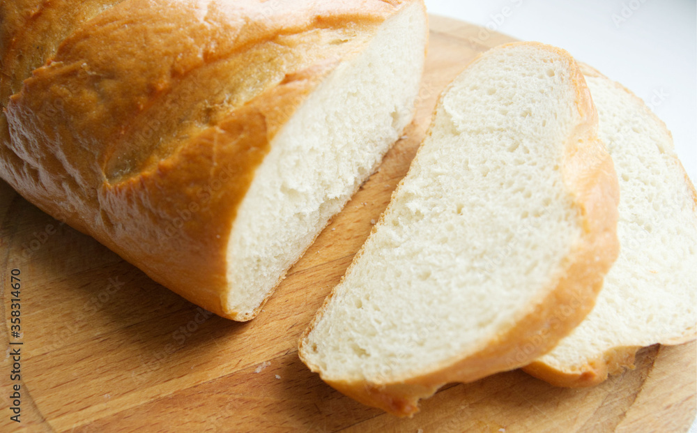 a loaf of white bread is sliced. White bread on a wooden board, on a light background. Bread texture, homemade cakes, cooking, breakfast, bakery.