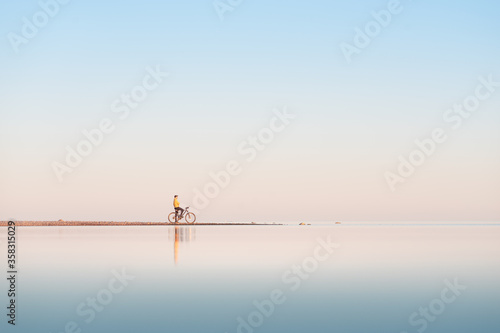 Cyclist on the shore of the calm sea. Distant plan.