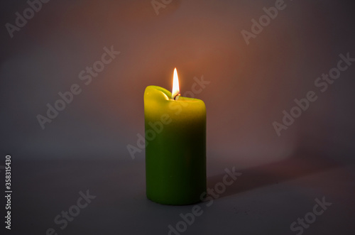 Big green candle on a dark background. The burning candle is yellow-green.