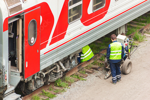 Railway workers repair a railway car.  Passenger wagon is under repair and is serviced by specialists.