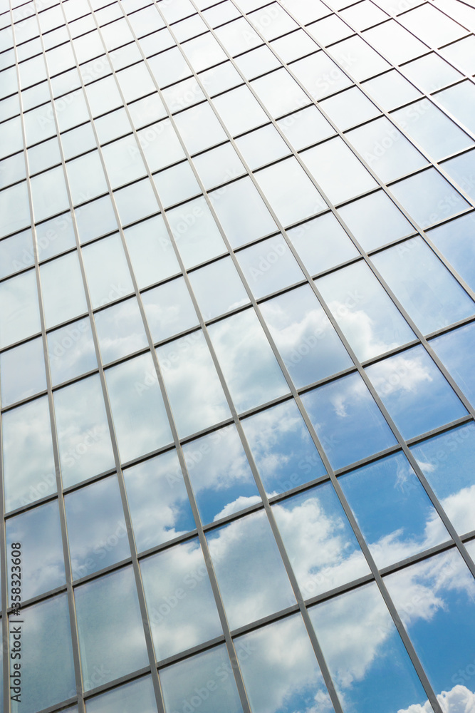 Clouds reflected in windows of modern office building. Facade texture of a glass mirrored office building. Clouds reflected in windows of modern office building. Facade texture of a glass mirrored office building.